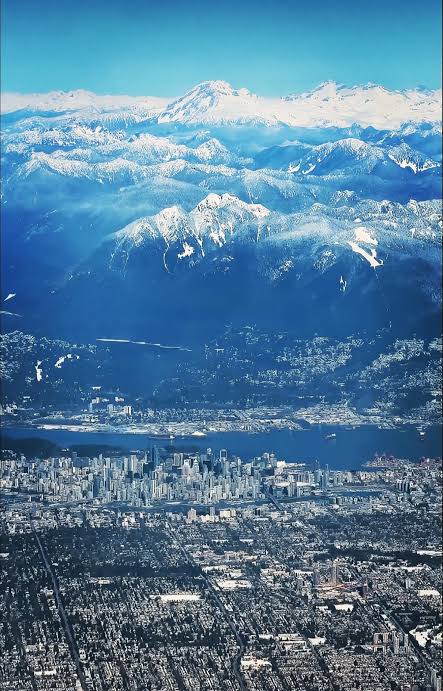 Downtown Vancouver seen from the air, with Burrard Inlet behind it and the snow-covered North Shore mountains above.
